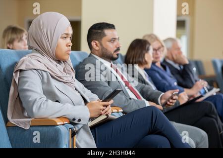 Groupe de professionnels multiethniques sérieux assis en auditorium et à l'écoute de la présentation lors de la conférence Banque D'Images