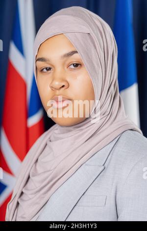 Portrait d'une femme politique sérieuse du Moyen-Orient dans le hijab se tenant contre des drapeaux internationaux Banque D'Images