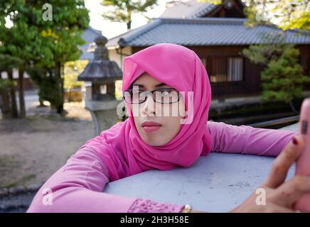 Gros plan de la jeune femme musulmane asiatique portant le hijab rose et des lunettes portant un smartphone.Expression épuisé faim, triste, endormi et fatigué Banque D'Images