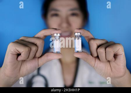 Une femme médecin tenant 2 flacons de vaccin en parallèle.Un médecin en manteau blanc et stéthoscope autour de son cou montrant 2 bouteilles en verre avec blanc W Banque D'Images