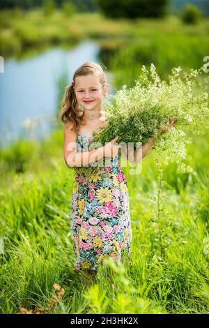 La petite fille est en piquant dans l'herbe et tient un bouquet Banque D'Images