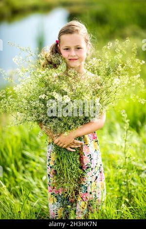 La petite fille est en piquant dans l'herbe et tient un bouquet Banque D'Images