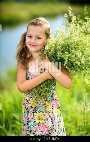 La petite fille est en piquant dans l'herbe et tient un bouquet Banque D'Images