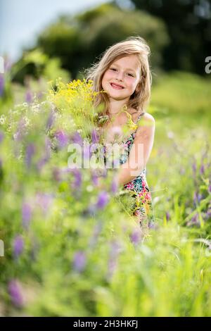 La petite fille est en piquant dans l'herbe et tient un bouquet Banque D'Images