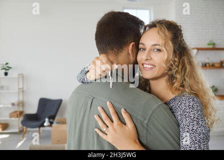 Bonne jeune femme embrassant son mari, tenant la clé de leur nouvelle maison et souriant Banque D'Images