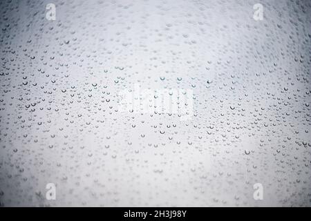 Gouttes de pluie sur le verre ou la fenêtre filmées en angle sur un arrière-plan clair et transparent.Textures d'automne, arrière-plans. Banque D'Images