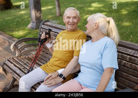 Homme senior heureux avec des bâtons pour la marche nordique et femme assis sur le banc dans le parc Banque D'Images