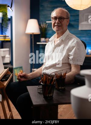 Artiste senior regardant la caméra assis dans un atelier d'art studio.Personne aînée caucasienne se préparant à recréer le chef-d'œuvre avec la conception de vase sur la table.Vieil homme avec créativité de dessin Banque D'Images