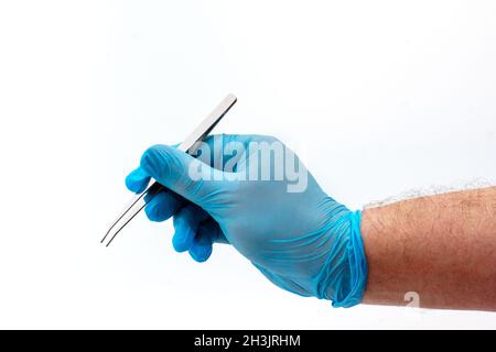 Main de l'homme dans un gant en latex bleu tenant une pince à épiler médicale en acier inoxydable isolée sur fond blanc. Concept de chirurgie opératoire. Sureur en plastique et cosmétique Banque D'Images