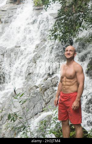 Joyeux homme beau debout et regardant près de la chute d'eau Banque D'Images