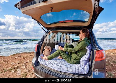 Une jeune femme avec un smartphone se repose dans une voiture au bord de l'océan. Banque D'Images