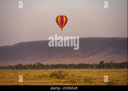 Montgolfière à rayures colorées avec des touristes survolant la savane au lever du soleil, Masa Mara, Kenya Banque D'Images