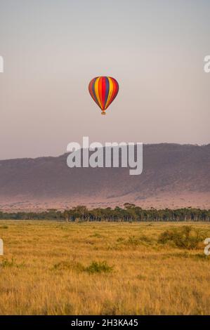 Montgolfière à rayures colorées avec des touristes survolant la savane au lever du soleil, Masa Mara, Kenya Banque D'Images