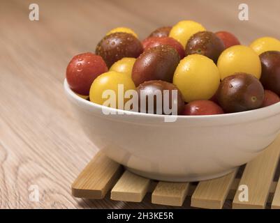 Les tomates cerise dans une variété de couleurs dans un bol en céramique sur fond de bois. Banque D'Images