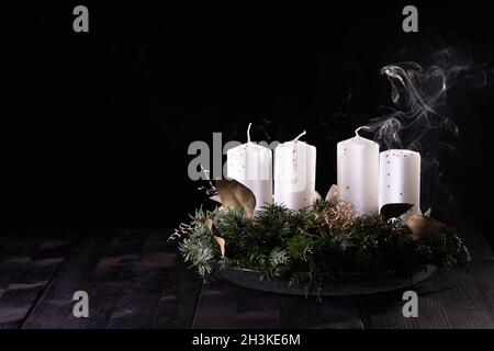 Premier Avent - couronne de l'Avent de branches de sapin et de vert permanent avec bougie soufflée sur une table en bois sombre.Fumée blanche sur fond noir, espace de copie. Banque D'Images