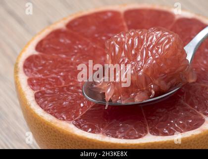 La moitié de pamplemousse rouge mûre juteuse avec tranche dans une cuillère. Vue en gros plan. Banque D'Images