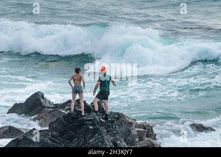 Quelques vacanciers prenant un risque et se tenant sur des rochers à Fistral, en Cornouailles. Banque D'Images