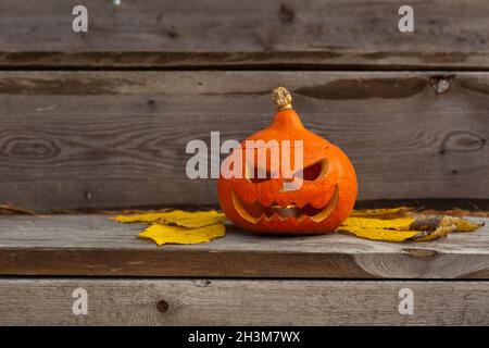 halloween citrouille effrayante avec les yeux et la bouche et les feuilles jaunes sur fond de bois.Citrouille d'automne Banque D'Images