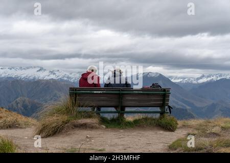 Un couple assis sur le banc, profitant de la vue sur le lac Wakatipu et les chaînes de montagnes de Queenstown, South Island Banque D'Images