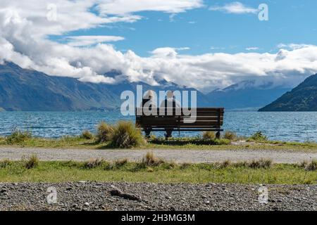 Un couple assis sur le banc, profitant de la vue sur le lac Wakatipu et les chaînes de montagnes de Queenstown, South Island Banque D'Images