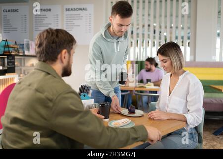 Un barista masculin sert des desserts frais et du café pour aller à l'homme et à la femme au café Banque D'Images