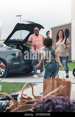 Père souriant et mère regardant son fils tout en chargeant ses bagages dans une voiture électrique Banque D'Images