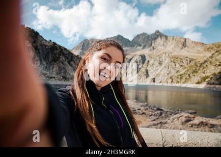 Fille prenant un selfie tout en souriant avec un lac en arrière-plan Banque D'Images