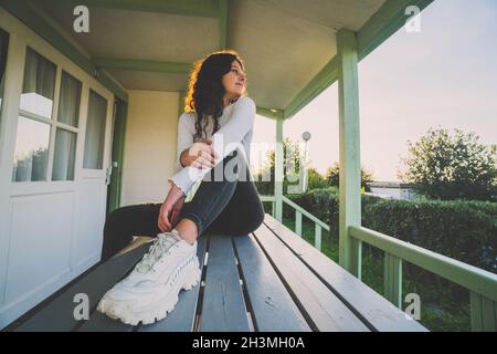 une femme assise à la table sur une terrasse d'un bungalow au coucher du soleil Banque D'Images