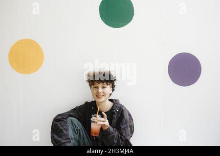 Portrait d'un adolescent souriant buvant contre des points de polka sur un mur blanc Banque D'Images