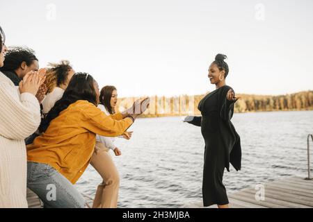 Des amies joyeuses applaudissent la femme dansant sur la jetée contre le ciel clair Banque D'Images