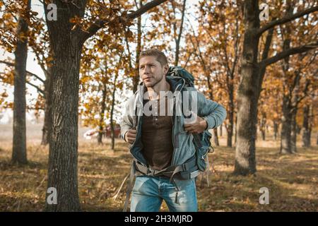 Tourisme au début du voyage.Un homme inspiré avec un grand sac à dos est sorti d'une voiture rouge et commence son voyage à travers Banque D'Images