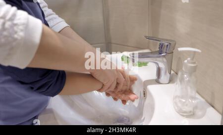 Se laver les mains avec maman.Gros plan.Les femmes aident à se laver le savon des mains sous le jet d'eau.Soins de santé Banque D'Images