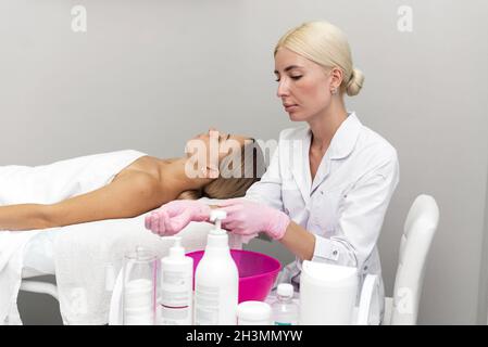 Une belle esthéticienne met des gants sur ses mains tandis que le client se trouve sur le canapé et attend la procédure. Banque D'Images
