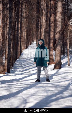 Une jeune femme se trouve sur la route parmi les arbres.Une femme caucasienne marche le jour ensoleillé de la neige givrée dans la forêt après une forte chute de neige Banque D'Images