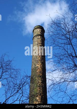 Vue verticale d'une vieille cheminée en pierre dans un moulin en ruines entouré d'arbres contre un ciel bleu nuageux dans la vallée de Colden ouest y Banque D'Images