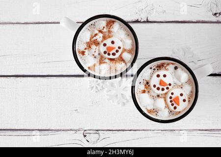 Deux tasses de chocolat chaud de vacances avec guimauves bonhomme de neige.Vue de dessus sur un fond en bois blanc. Banque D'Images