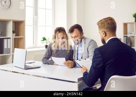 Clients assis à un bureau dans le bureau de l'agent immobilier et lisant le contrat qu'il leur a donné Banque D'Images