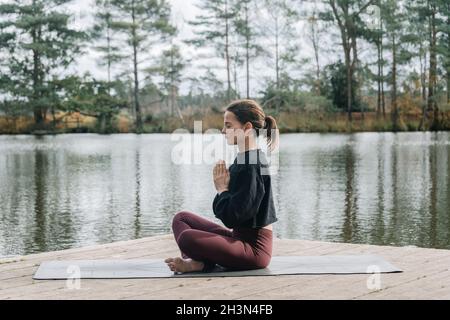 Femme assise à côté d'un lac traversé à pattes et méditant.Pratiquer le yoga à l'extérieur. Banque D'Images