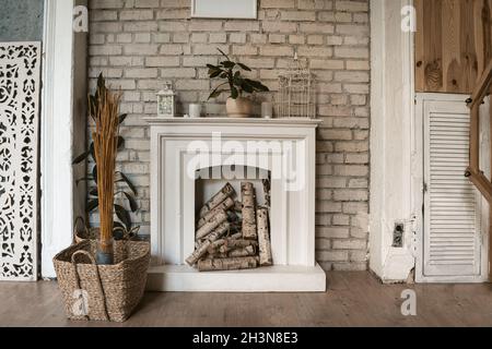 Cheminée blanche dans un mur de briques.Il y a du bois dans la cheminée.Panier en osier à proximité avec plantes sèches décoratives.PH de haute qualité Banque D'Images