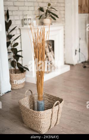 Bâtonnets secs dans un vase et un panier en osier. En arrière-plan se trouve une cheminée blanche et un mur de briques. Photo de haute qualité Banque D'Images