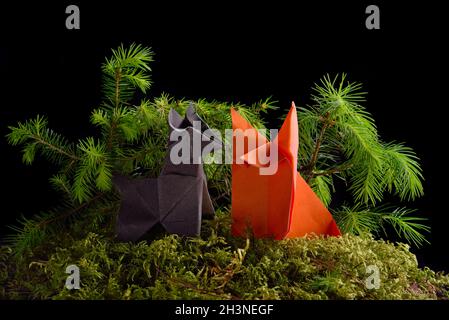 Le loup et le renard en papier origami sur des mousses vertes isolées sur fond noir Banque D'Images