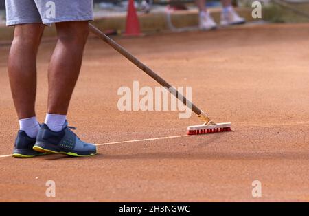 Un homme méconnaissable nettoie la ligne de marquage du court de tennis en argile avec une brosse spéciale.Nettoyage de courts de tennis en terre battue.Maintenance et préparation Banque D'Images