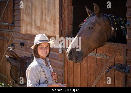 Petite fille pilote communique avec le cheval après le sport équestre.La mare brune peeks hors de stable de manière amicale.Animaux Banque D'Images