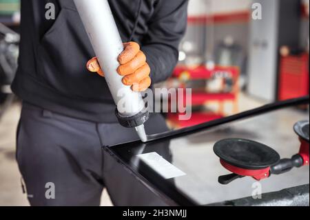 Vitrier appliquant du joint en caoutchouc sur le pare-brise dans le garage, gros plan. Banque D'Images