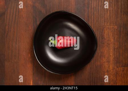 Mini poivron rouge dans un châle noir isolé sur fond en bois. Vue de dessus Banque D'Images