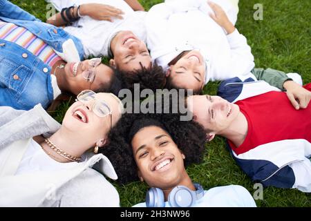Groupe d'amis qui rient dehors allongé sur l'herbe, partageant une bonne et positive humeur. Banque D'Images