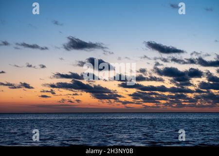 Vue sur le soleil couchant qui brille sur la mer et se reflète sur la plage, nuages avec des bords ensoleillés.Paysage Banque D'Images