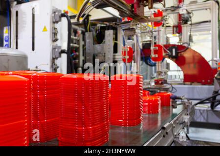 Machine d'usine plaçant des couvercles en plastique rouge sur le tapis convoyeur.Technologie industrielle pour les récipients alimentaires, concepts de fabrication Banque D'Images