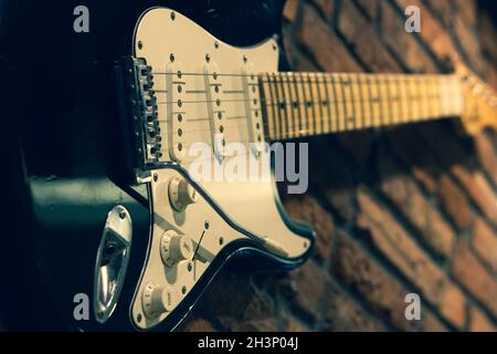 Gros plan sur une guitare noire et blanche accrochée sur un mur de briques.Décoration de magasin de musique concept, effet vintage Banque D'Images