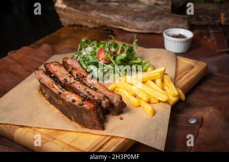 Côte de bœuf avec frites et salade d'arugula avec tomates cerises et parmesan servis à bord recouverts de pa de qualité alimentaire Banque D'Images